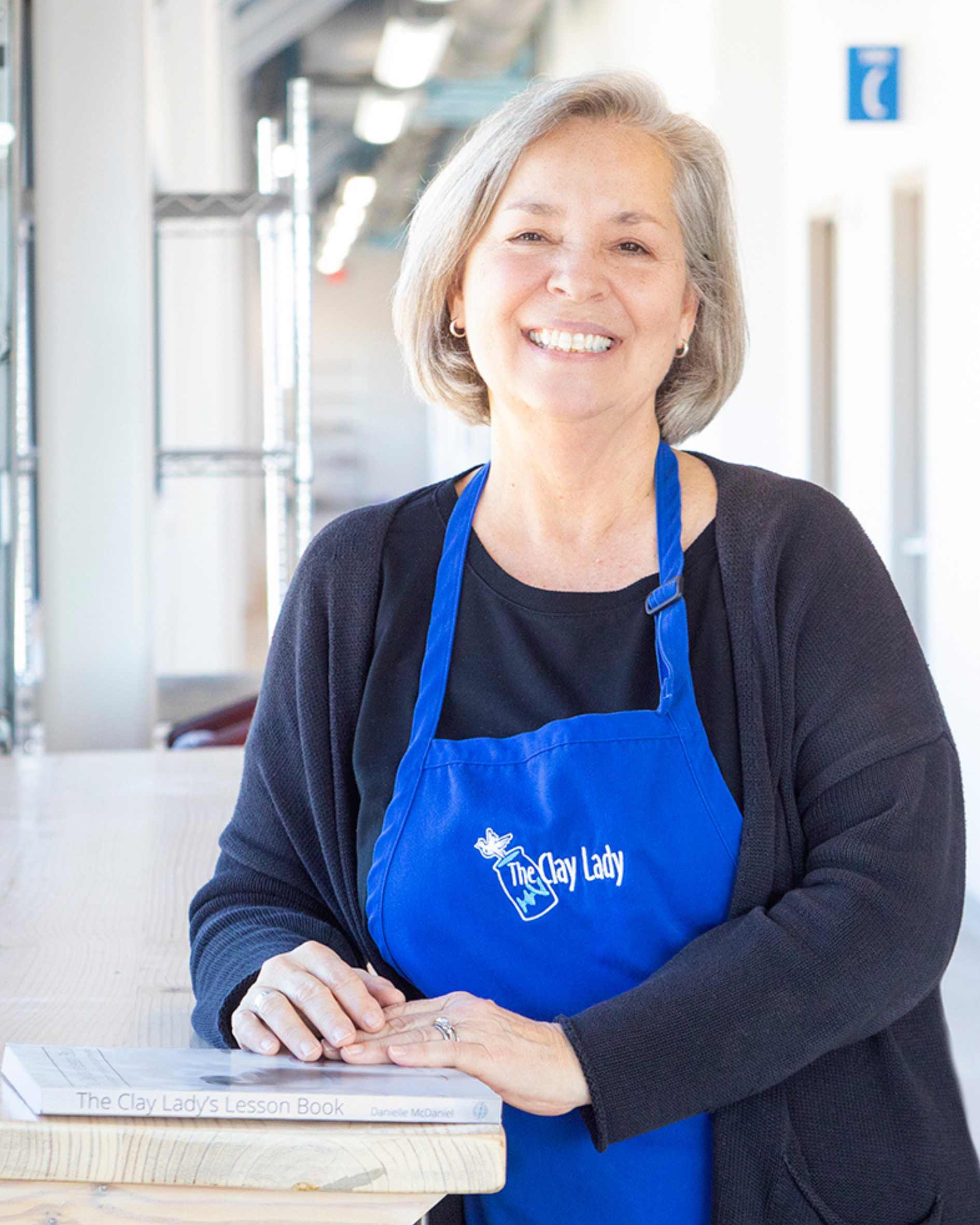 Danielle McDaniel, wearing a blue apron with gray hair and stands.